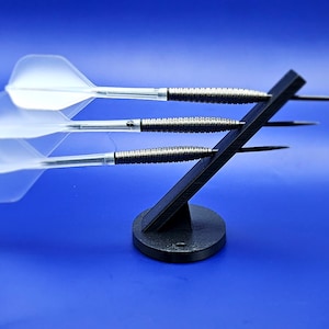 May include: Three silver darts with white flights are displayed on a black stand. The stand has a round base and a triangular top.