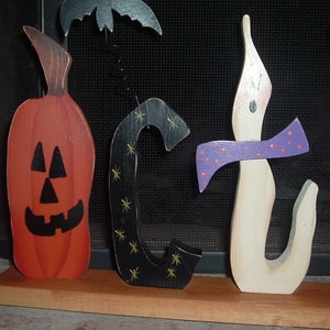 May include: Wooden Halloween decorations spelling out "OCT" with a pumpkin, a black letter "C" with gold stars, and a candle with a purple bow. The pumpkin is orange with a carved face. A black bat is above the letters.