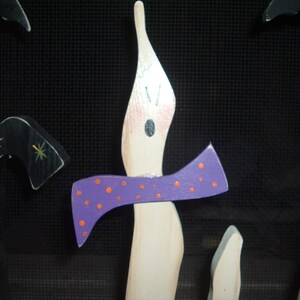 May include: Wooden Halloween decorations featuring a candle with a purple bow and orange polka dots. Other decorations include a black bat and a black candy cane shape with gold stars. The background is black.