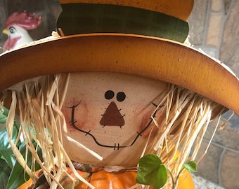 Può includere: Statuetta decorativa di spaventapasseri con volto dipinto, capelli di paglia e cappello a tesa larga. Il cappello è marrone con una fascia verde. Lo spaventapasseri ha un corpo arancione e una sciarpa a quadri. Decorazione a tema autunnale.