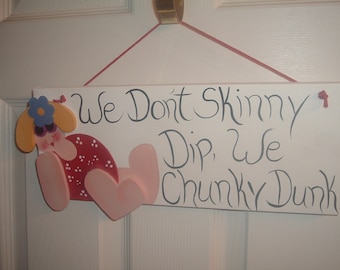 Peut inclure: Une pancarte en bois avec une fille de dessin animé en maillot de bain et le texte "We Don't Skinny Dip, We Chunky Dunk".