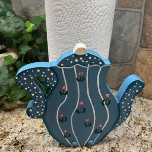 May include: Blue teapot-shaped paper towel holder with white polka dots and red flowers painted on it.