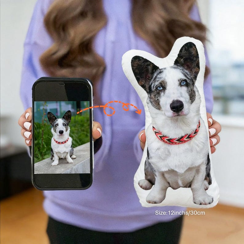 May include: A custom-shaped dog pillow featuring a photo of a dog with blue eyes and a red and black collar. The pillow is held next to a smartphone displaying the same image. The pillow measures 12 inches (30cm).