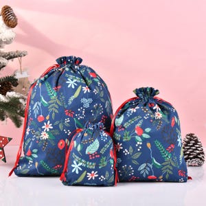 May include: Three blue drawstring bags with a floral pattern in red, white and green. The bags are made of fabric and have red drawstrings.
