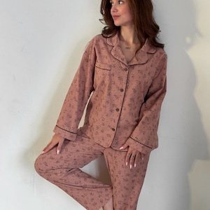 May include: A pink pajama set with a floral print. The top has a collared neckline and long sleeves. The pants have a straight leg.