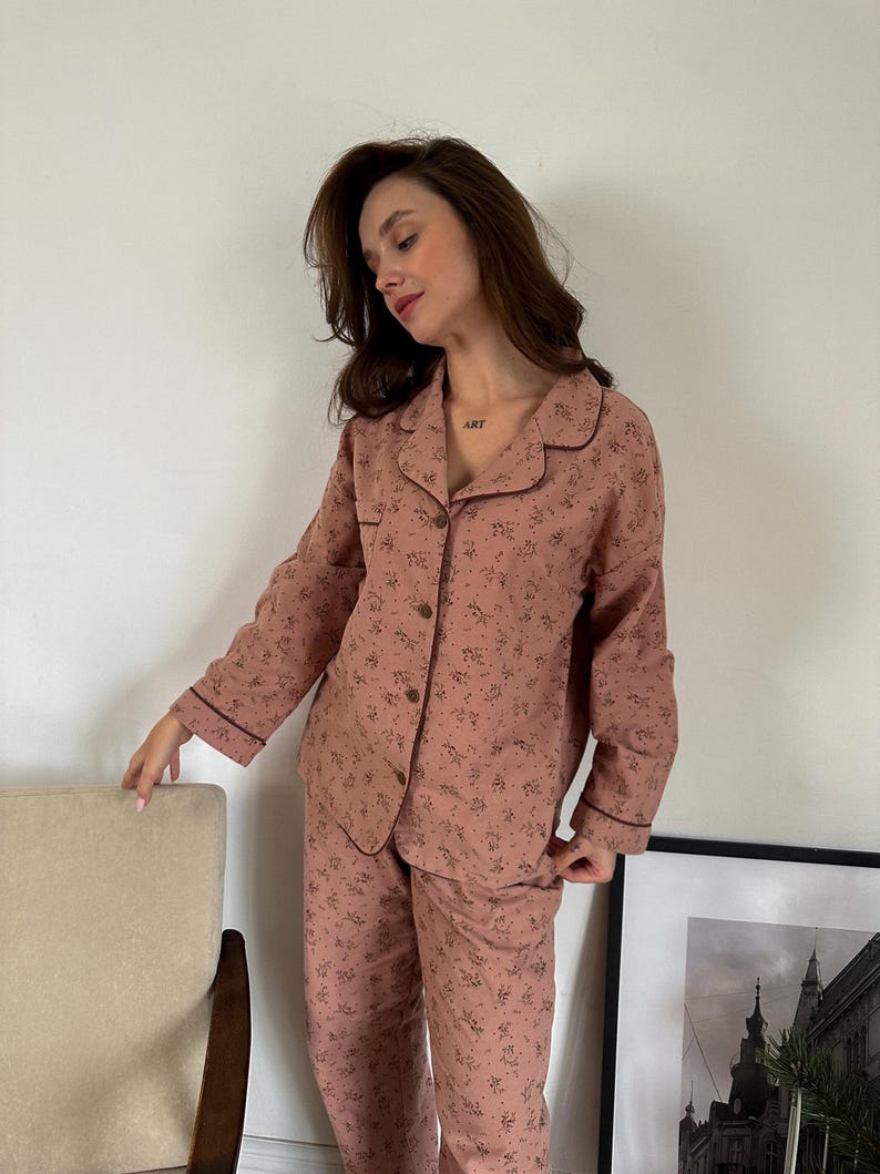 May include: A pink pajama set with a floral print and brown trim. The top has a collared neckline and long sleeves. The pants have a straight leg.