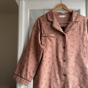 May include: A pink pajama set with a floral print and brown trim. The top has a button-up front and a collar. The pants have a drawstring waist.