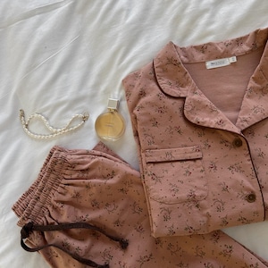 May include: A pink and brown floral pajama set with a drawstring waist and a button-up top. The top has a small pocket on the left side and a "Sense" label on the right side.