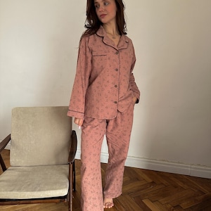 May include: A pink pajama set with a floral print and brown trim. The top has a collared neckline and long sleeves. The pants have a straight leg.