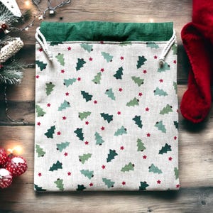 以下が含まれることがあります： 白い背景に、クリスマスをテーマにした巾着袋。緑のクリスマスツリーと赤い星の繰り返し模様が特徴です。袋の上部は緑色で、紐は白色です。
