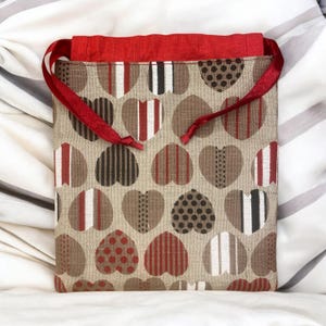 May include: A red drawstring bag with a beige fabric base. The fabric has a pattern of red, white and black hearts.