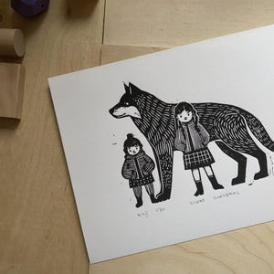 Peut inclure: Gravure sur linoléum en noir et blanc d'un loup avec deux enfants debout à côté de lui. L'impression est intitulée "Silent Guardians" et numérotée 6/20.