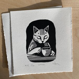 K&ouml;nnte beinhalten: Schwarz-wei&szlig;er Holzschnitt eines Katers, der Kaffee trinkt. Der Druck ist signiert und nummeriert 3/50.