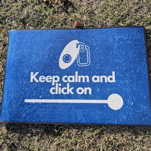 May include: Blue rectangular doormat with the text "Keep calm and click on" in white. The mat features a white graphic of a key and a tag. A white line leads to a white circle.
