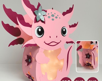 Könnte beinhalten: Eine rosa Axolotl-Laterne aus Papier mit dunkelrosa Kiemen, einer silbernen Glitzerblume und einem leuchtenden Zentrum. Das Design zeigt florale Ausschnitte an den Seiten sowie die Dateiformat-Symbole für PDF, SVG und PNG.