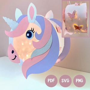 Può includere: Una lanterna di carta cilindrica a forma di testa di unicorno con un corno glitterato argento, criniera di carta rosa e viola e un grande occhio blu. La lanterna è illuminata dall'interno, diffondendo una luce calda attraverso i ritagli.