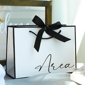 May include: White gift bag with a black ribbon and the word "Area" printed on the front.