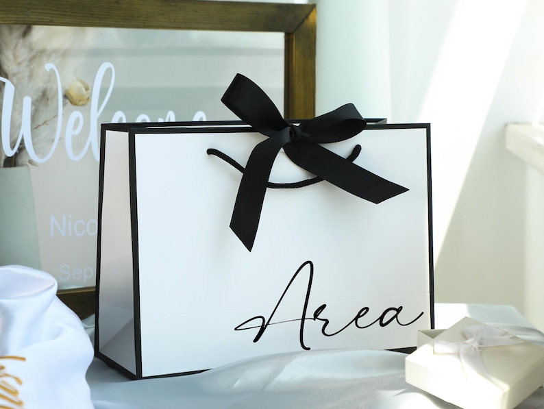 May include: White gift bag with a black ribbon and the word "Area" printed on the front.