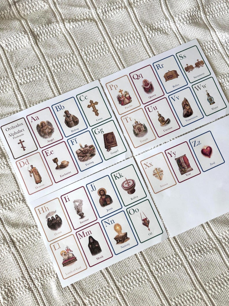 May include: Set of Orthodox Alphabet flashcards. Each card features a letter of the alphabet with an associated word and illustration. The cards are arranged on a white surface with a textured pattern. The text "Orthodox Alphabet Flashcards" is visible.