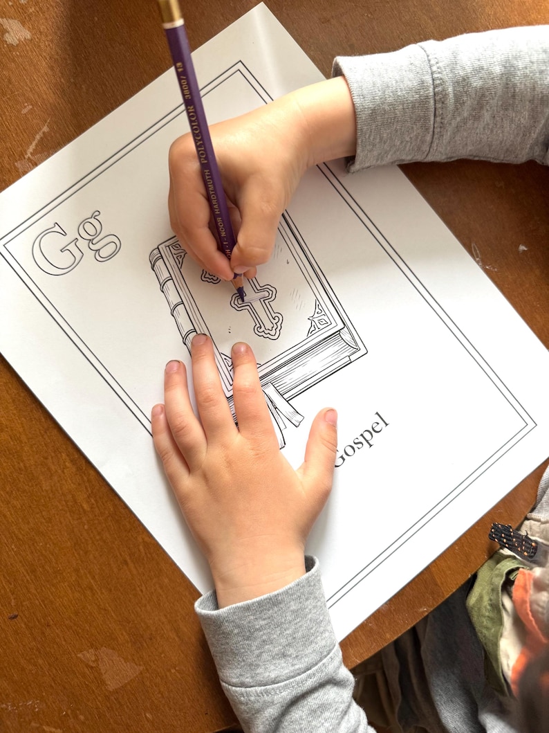 May include: A child's hands coloring a Gospel-themed coloring page with a purple pencil. The coloring page features the letter "G" and an illustration of a book with a cross on the cover. The word "Gospel" is printed on the page.