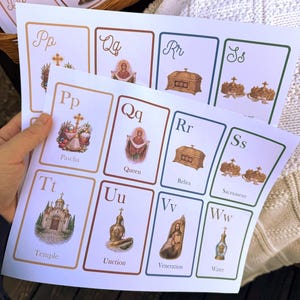 May include: Cards with religious illustrations and lettering. The cards feature images of a temple, relics, and a queen, with corresponding letters and words like "Pascha" and "Sacrament". The cards are held in a person's hand.
