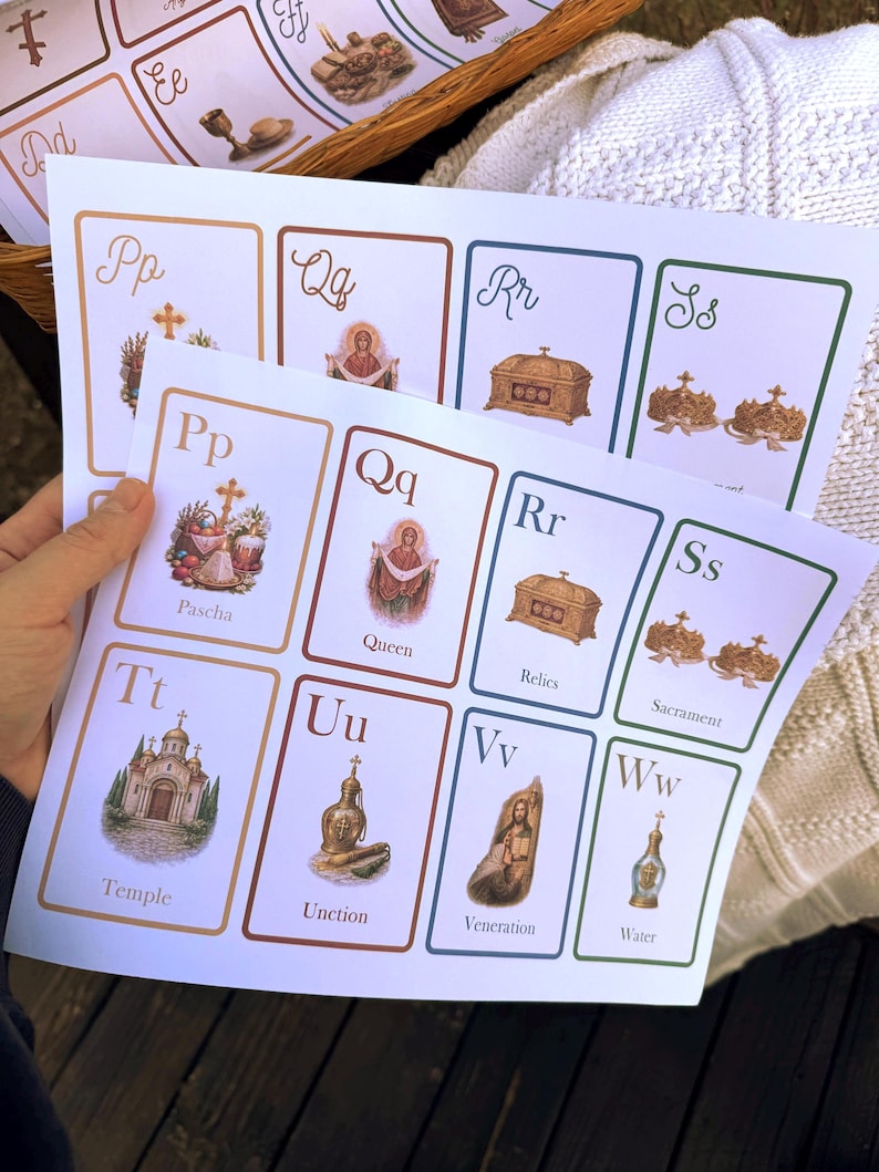May include: Cards with religious illustrations and lettering. The cards feature images of a temple, relics, and a queen, with corresponding letters and words like "Pascha" and "Sacrament". The cards are held in a person's hand.