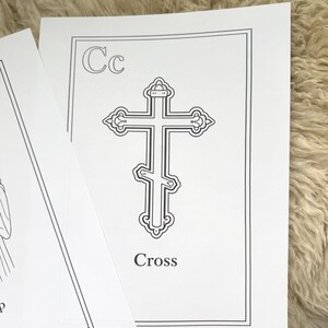 May include: A black and white illustration of a cross on a white card. The card has the letter "Cc" in the upper left corner and the word "Cross" at the bottom. The card is on a textured, light-colored surface.