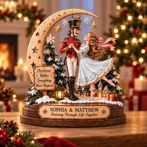 Puede incluir: Una figura decorativa de mesa que muestra a un cascanueces y una bailarina bailando bajo una luna creciente. La base muestra el texto 'SOPHIA & MATTHEW Dancing Through Life Together' y un letrero dice 'Christmas Makes Everything More Magical'.