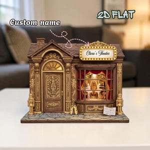 Puede incluir: Un detallado teatro en miniatura marrón con detalles dorados, con un letrero que dice "Clara's Theater". La fachada incluye una puerta, una ventana con cortinas rojas y un escenario con figuras de bailarinas. Se puede agregar un nombre personalizado.