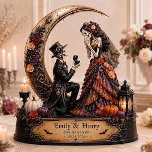May include: A decorative figurine featuring two skeletons, one kneeling in a tuxedo and top hat offering a ring to the other in a ruffled gown and veil. They stand before a large crescent moon adorned with roses, with a base inscribed: Emily & Henry, SHE SAID YES, 10.31.2026.