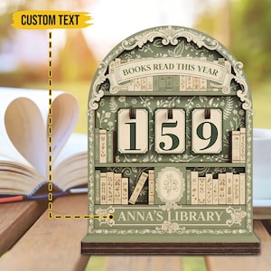 May include: A green wooden book counter in the shape of a bookshelf, displaying "BOOKS READ THIS YEAR" and the number "159". It features floral and book motifs, with the text "ANNA'S LIBRARY".