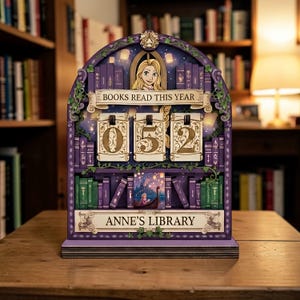 Könnte beinhalten: Ein holzfarbener Kalender in Form eines Bücherregals mit dem Text „BOOKS READ THIS YEAR“ und „ANNE'S LIBRARY“. Der Kalender zeigt die Zahl „052“. Das Design zeigt eine Cartoon-Zeichnung einer Frau mit langen blonden Haaren und eine Bootszene.
