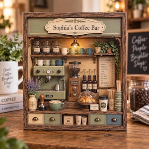 May include: A miniature wooden coffee bar display titled Sophia's Coffee Bar, featuring a green espresso machine, a coffee grinder, syrup bottles, a menu board, small mugs, a pastry stand with croissants, and drawers with brass-toned knobs.
