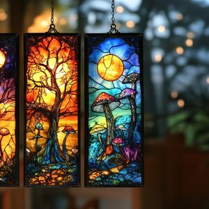 May include: Three stained glass panels with fantastical scenes. One shows a crescent moon over a tree, another a tree with a setting sun, and the third features mushrooms under a full moon. Each panel has a black frame and is suspended by a chain.