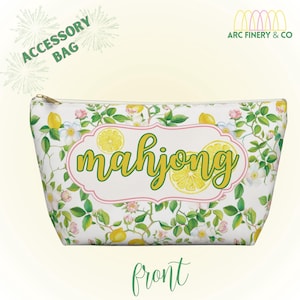 Op de afbeelding: Witte accessoiretas met een citroen- en bloemenpatroon. De tas heeft het woord "mahjong" in een groen scriptlettertype, omlijnd door een roze rand. De tas heeft een gouden rits en de tekst "Accessory Bag" is zichtbaar.
