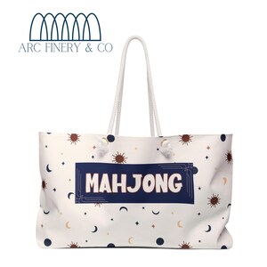Può includere: Borsa tote in tela bianca con un rettangolo blu navy che dice "Mahjong" in lettere bianche. La borsa ha un manico in corda bianca e uno sfondo bianco con un motivo di stelle, lune e soli.