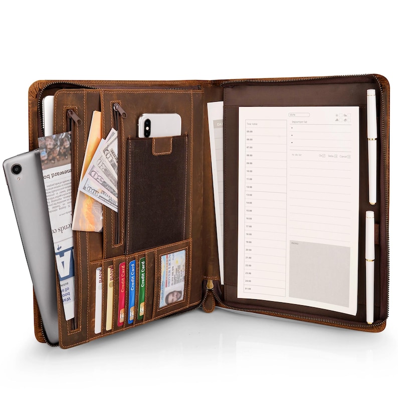 May include: Open brown leather zippered portfolio with a notepad, pen, and multiple pockets. The portfolio has a phone pocket, a zippered pocket, and a slot for credit cards. The notepad has a lined page with a blank space at the bottom for notes.