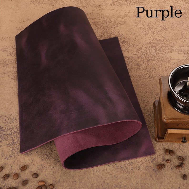 May include: A sheet of purple leather with a textured surface, folded over to reveal a lighter purple underside. The word "Purple" is in the upper right corner. Coffee beans and a wooden coffee grinder are in the background.