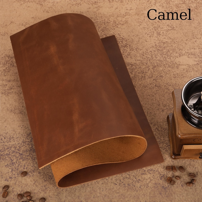 May include: A rolled sheet of camel-colored leather with a visible grain. The leather has a rich, brown hue with lighter undertones. The word "Camel" is printed in black in the upper right corner. The leather is likely for crafting or upholstery.