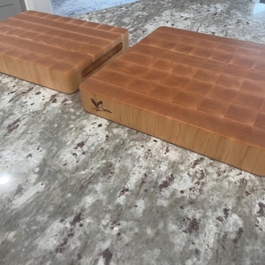 May include: Two wooden chopping boards with a grid pattern on the surface. The boards are made of light brown wood and have a natural finish. The boards are both rectangular in shape and have a small bird logo on the side.