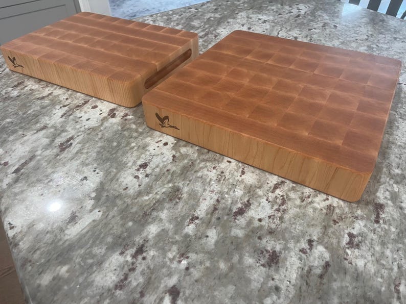 May include: Two wooden chopping boards with a grid pattern on the surface. The boards are made of light brown wood and have a natural finish. The boards are both rectangular in shape and have a small bird logo on the side.