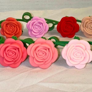 May include: A collection of colorful rose-shaped bottle stoppers. The stoppers are in various shades, including red, pink, and white, with green stems. These decorative items are designed to add a floral touch to wine bottles.