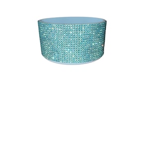 Puede incluir: Un objeto cil&iacute;ndrico azul claro con un borde y una base. El exterior est&aacute; cubierto de peque&ntilde;os y brillantes pedrer&iacute;a azul claro. El objeto parece ser un art&iacute;culo decorativo.