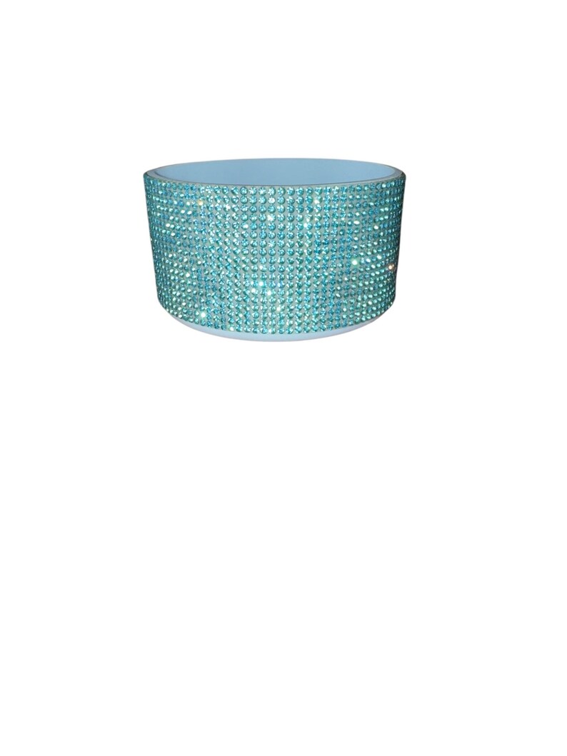Puede incluir: Un objeto cil&iacute;ndrico azul claro con un borde y una base. El exterior est&aacute; cubierto de peque&ntilde;os y brillantes pedrer&iacute;a azul claro. El objeto parece ser un art&iacute;culo decorativo.