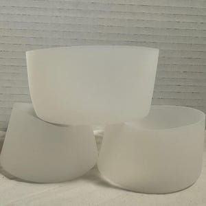 May include: Three frosted glass bowls are stacked in a close-up shot. The bowls have a smooth, curved design and a soft, translucent appearance. The bowls are white and have a modern, minimalist aesthetic.