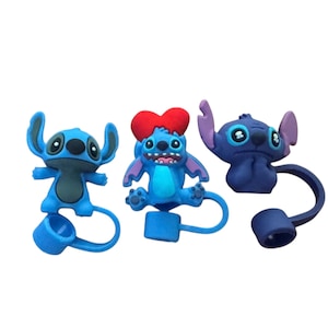 May include: Three blue cartoon character bottle stoppers. One has a red heart-shaped bow, another a sad expression, and the third a happy expression. Each stopper has a blue loop and cap.
