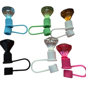 May include: A collection of colorful bottle stoppers with diamond-shaped tops. The stoppers come in various colors, including blue, green, white, black, clear, and pink. Each stopper has a matching loop and a square base.