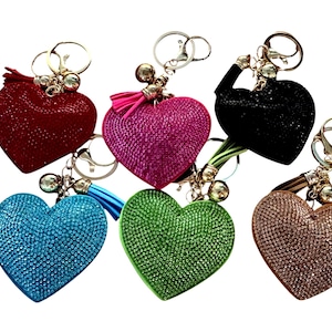 May include: Six heart-shaped keychains in various colors: red, pink, black, blue, green, and bronze. Each keychain is covered in small, sparkling embellishments and has a tassel and a metal keyring.