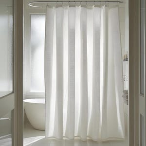 Puede incluir: Una cortina de ducha blanca con rayas verticales texturizadas cuelga en un ba&ntilde;o. La cortina est&aacute; suspendida de una barra de metal curvada. Se ve una ba&ntilde;era blanca a trav&eacute;s de la ventana.