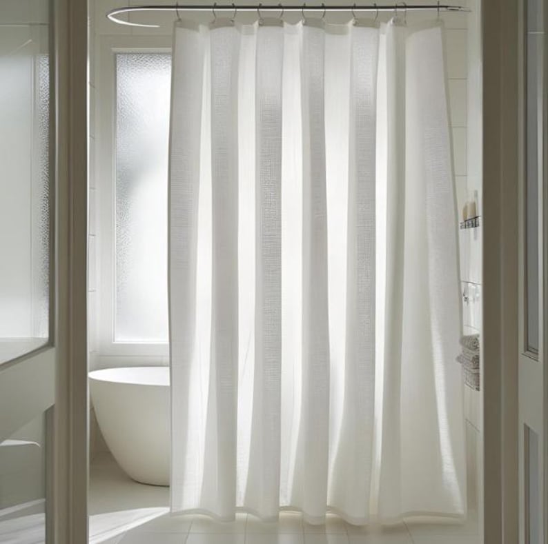 Puede incluir: Una cortina de ducha blanca con rayas verticales texturizadas cuelga en un ba&ntilde;o. La cortina est&aacute; suspendida de una barra de metal curvada. Se ve una ba&ntilde;era blanca a trav&eacute;s de la ventana.
